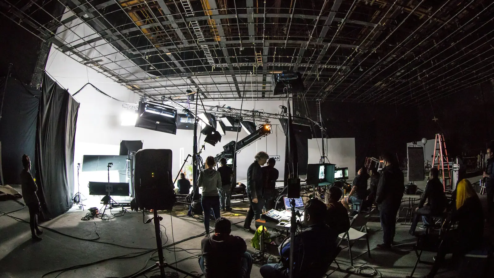 A film crew on a soundstage, lighting rig and stands set around the camera position.